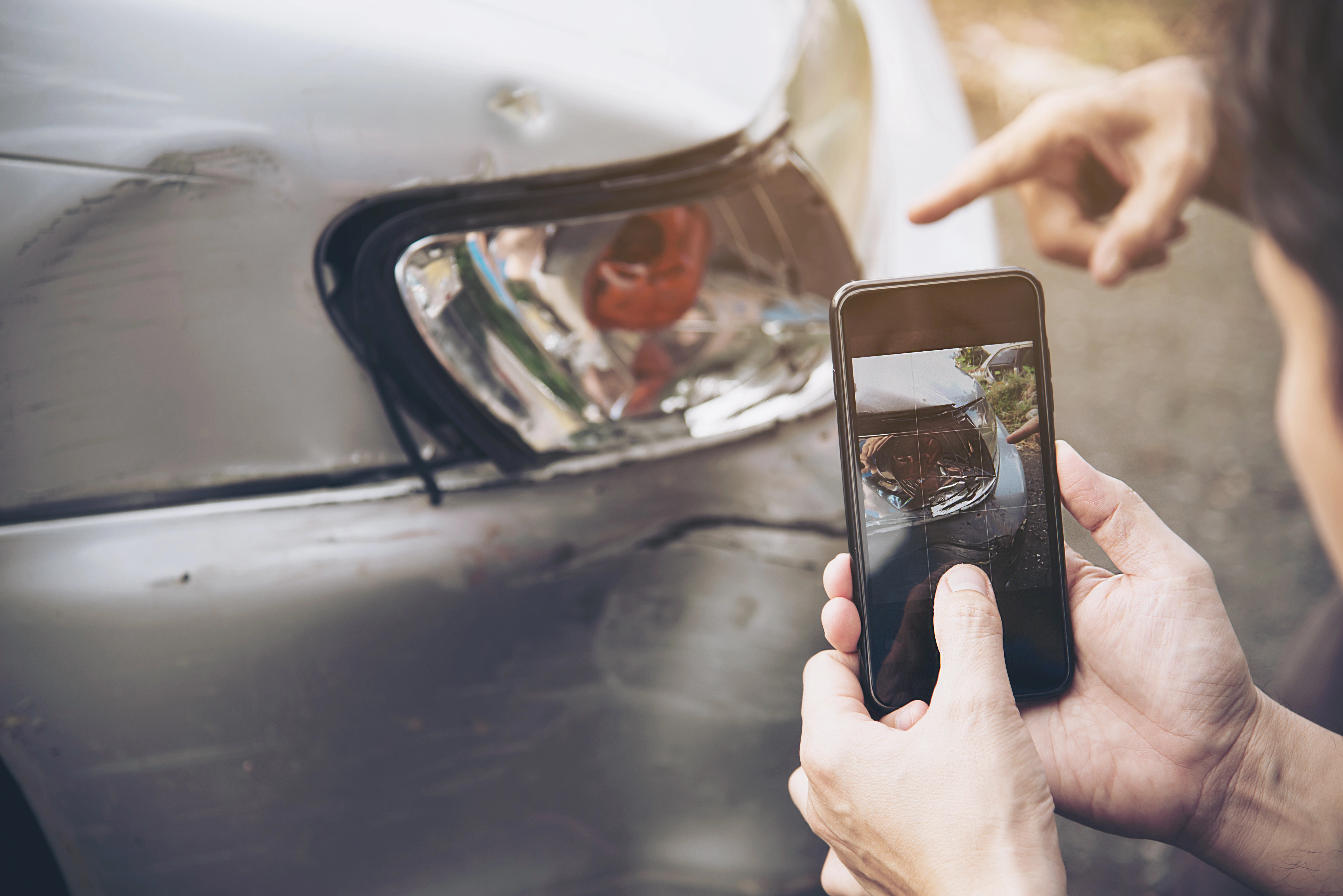 uomo che fotografa con lo smartphone i danni alla carrozzeria di un'auto usata per documentare un possibile incidente non dichiarato