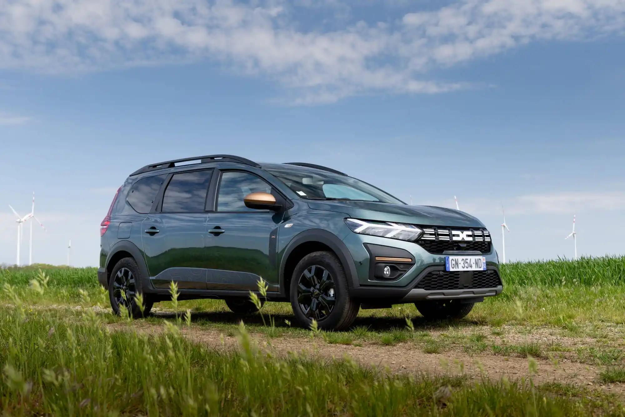 Nuova Dacia Jogger 7 posti color verde scuro su strada di campagna, SUV familiare spazioso ed economico ideale per grandi famiglie, con design moderno e versatilit&agrave; per viaggi lunghi.